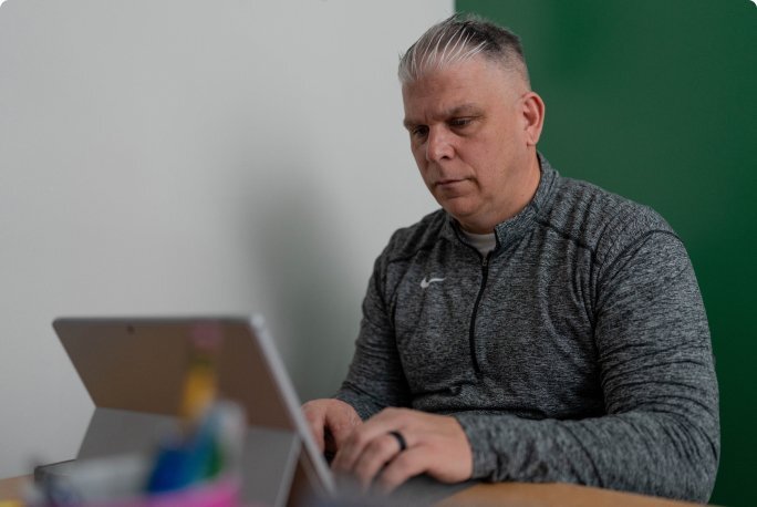 Athletic director sitting at desk typing on a laptop.