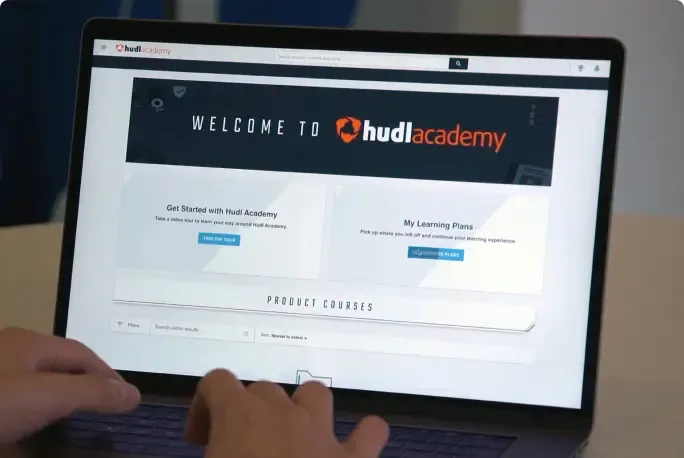 A persons hands resting on a laptop keyboard while browsing the Hudl Academy website.