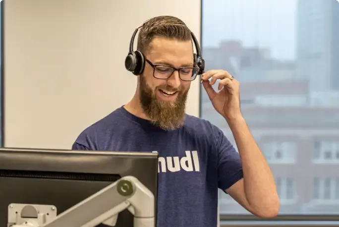 A Hudl service agent talking with a headset at a standing desk with a monitor.
