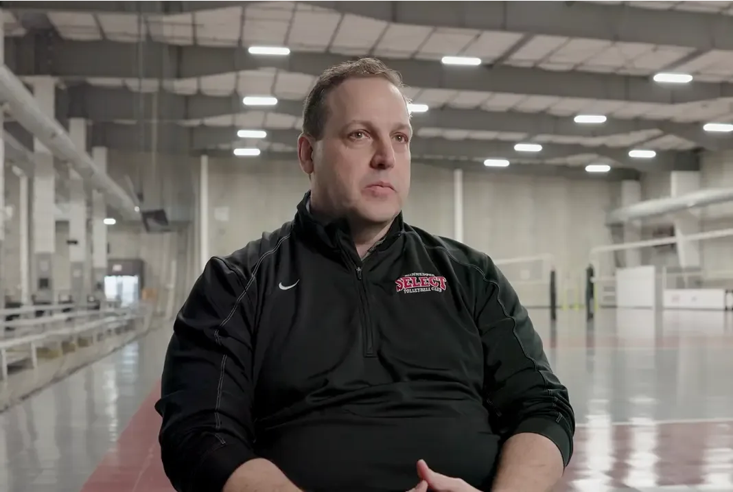 A man in a blue and gray jacket looks thoughtfully to the side.