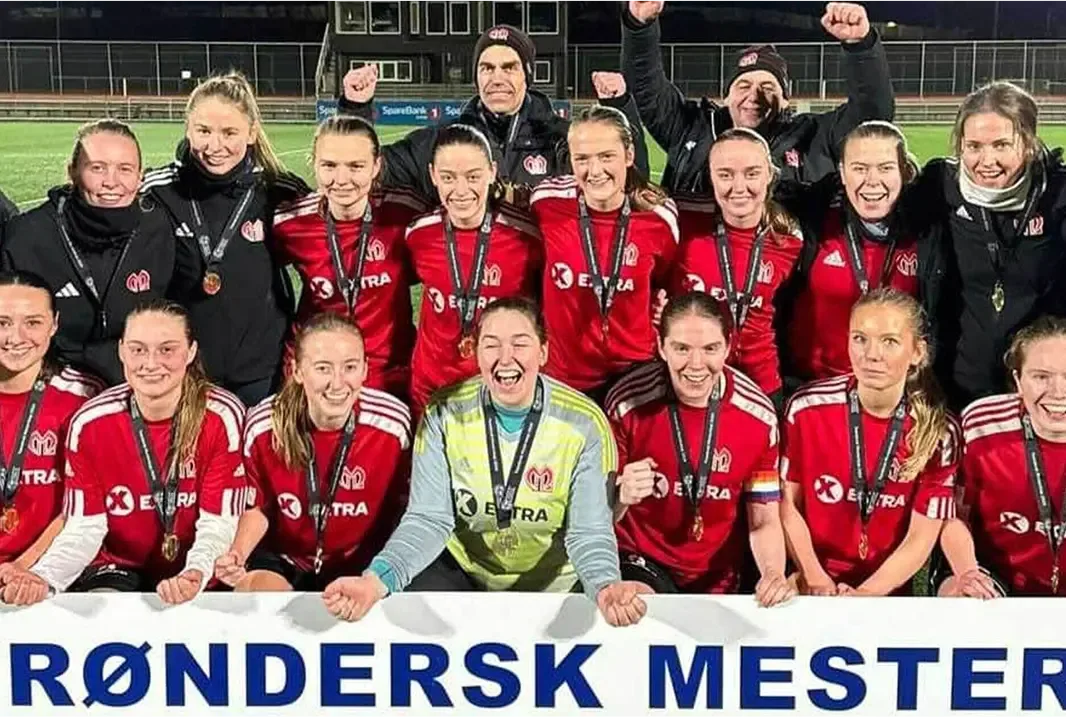 A soccer team, Malvik IL, celebrates their championship win with medals and a banner.