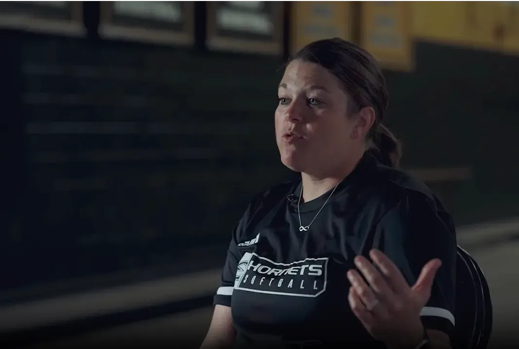 April Rosales, the Emporia State softball coach, speaks while sitting in front of a dark wall.
