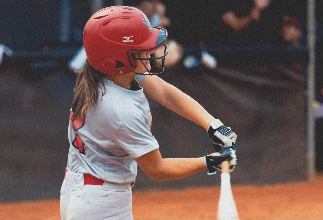 A softball player in a red helmet and a gray and red uniform swings a bat.